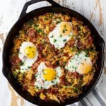 Cast-iron skillet hash topped with four sunny-side-up eggs and herbs