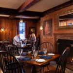 Cozy wood-paneled restaurant dining room with a glowing fireplace