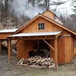 Wood-fired Vermont sugarhouse steaming beside a pile of split firewood