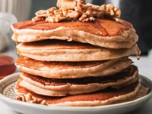 Stack of pancakes topped with walnuts and glossy maple syrup
